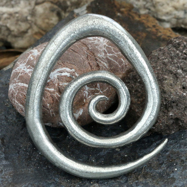 The SPIRAL Minimalist Ear Hangers in Silver by Kaya Movement, handcrafted with a rustic and artistic design, are placed on a dark, textured stone surface. The 0 gauge ear hangers stand out beautifully against the natural background.